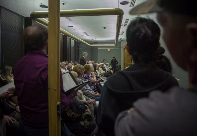 A crowd of people listen to a speaker in a public meeting room.