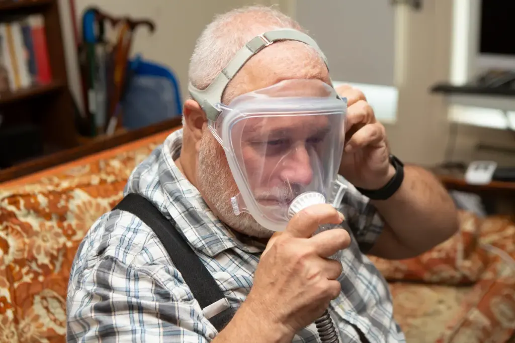 An older man puts on an oxygen mask that is connected to a medical device for sleep apnea.