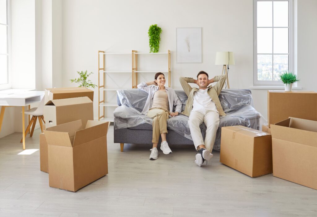 Smiling,Couple,Relaxing,On,Sofa,,Moving,Boxes.,In,An,Apartment